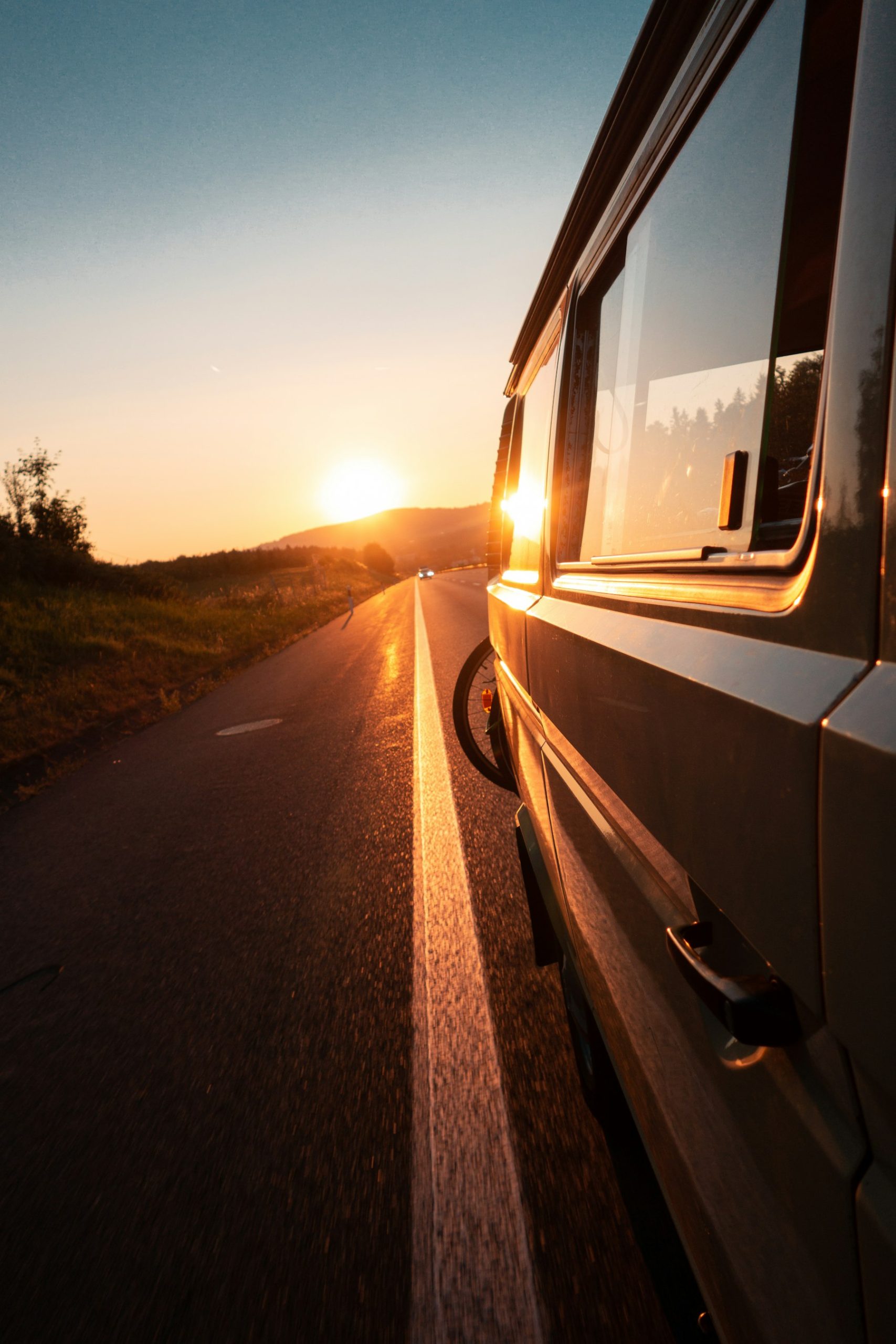 Lateral de uma autocaravana parada na berma de uma estrada ao fim da tarde, com o sol baixo em frente